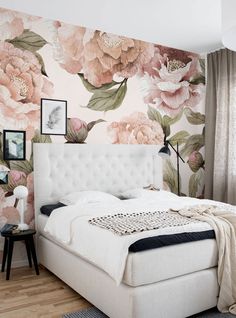 a white bed sitting in a bedroom next to a wall covered in pink and green flowers