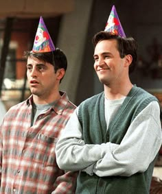 two men standing next to each other wearing party hats