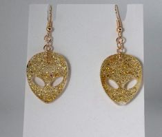 Add a touch of cosmic charm to your look with these Gold Sparkle Mini Alien Head Dangle Earrings! Handmade with epoxy resin, these unique earrings are filled with lots of gold sparkles, making each pair truly one of a kind. A perfect gift for alien lovers or anyone who loves a little extraterrestrial flair in their jewelry collection. Details: About 1 inch diameter All items are handmade, if an item has more than (1) in stock, they were poured from the same batch of epoxy resin. Please note: the Alien Head, Earrings Unique, Gold Sparkle, Handmade Gold, Unique Earrings, Epoxy Resin, Favorite Things Gift, Earrings Handmade, Jewelry Earrings Dangle