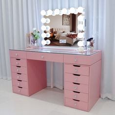 a pink vanity with lighted mirror and drawers