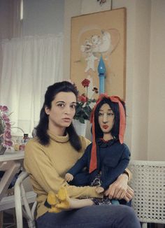 a woman sitting on top of a chair next to a doll wearing a hoodie