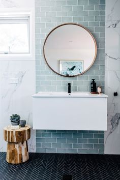 a white sink sitting under a round mirror next to a wooden stool in a bathroom