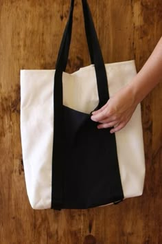 a person holding a black and white bag on top of a wooden floor next to a wall