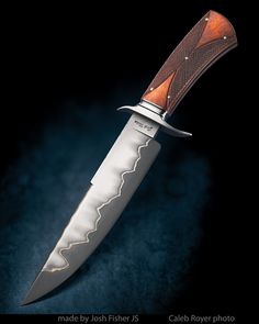 a knife that is on top of a black surface with an intricate pattern and wooden handle