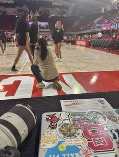 a woman kneeling on the floor in front of a basketball court with people standing around