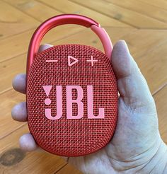 a hand holding a red jbl portable speaker