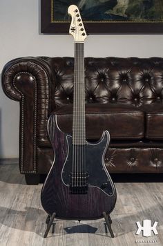 an electric guitar sitting on top of a wooden stand in front of a brown couch