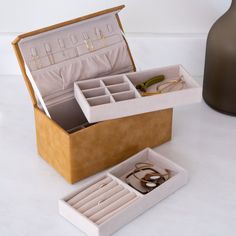 an open jewelry box sitting on top of a white table next to a brown vase