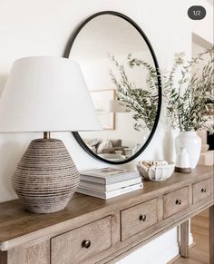 a table with a lamp and mirror on it next to a dresser in a living room