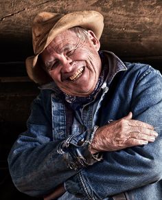 an old man wearing a cowboy hat is smiling and holding his arms crossed in front of him