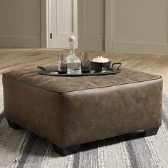 a brown ottoman sitting on top of a wooden floor next to a table with drinks