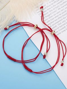 two red string bracelets with silver beads on top of a blue surface next to an open book