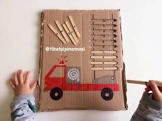 a child holding a pencil in front of a cardboard box with wooden pegs on it