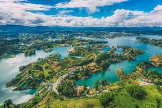 an aerial view of a lake surrounded by lush green hills and trees with blue skies in the background