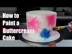 someone is decorating a cake with pink, blue and white icing on it