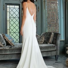 a woman in a white wedding dress standing next to a couch and looking off into the distance