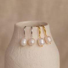 Fall in love with the timeless beauty of our Dangling Pearl Drop Earrings. With their graceful design and lustrous pearls, these earrings capture the essence of romance and are perfect for completing your summer wedding look or embracing a minimalist boho style. Material: High Quality Solid 925 Sterling Silver Finish: Sterling Silver ∙ 18K Gold Featuring ~16.5mm Hook Earrings with ~10 x 8.5mm Dangling Pearl Charm Sold as a pair Model showcases a summery, romantic look featuring Vera Pave Huggies Initial Tag Necklace, Wedding Look, Romantic Look, Bar Bracelets, Pearl Charms, Birthstone Necklace, Pearl Drop Earrings, Pearl Drop, Hook Earrings