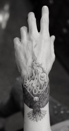 a hand with an eagle tattoo on it's wrist and the arm is covered in flames