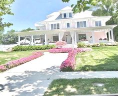 a large white house sitting on top of a lush green field covered in pink flowers