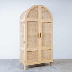 an arched wooden cabinet with wicker doors on the top and bottom, against a white wall