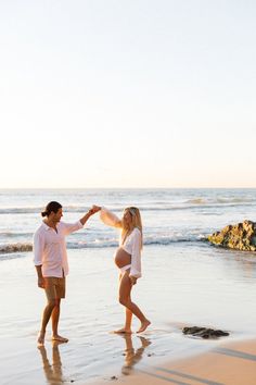 a man and woman standing on top of a beach next to the ocean holding hands