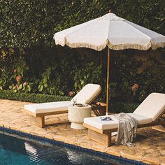 two chaise lounge chairs next to a pool with an umbrella and towel on it