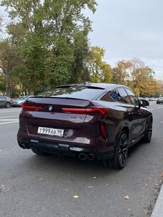 the rear end of a brown bmw suv parked on the side of the road in front of some trees