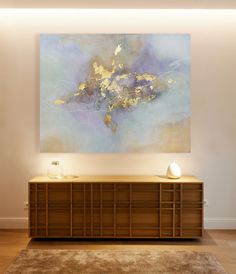 an abstract painting hangs on the wall above a large wooden cabinet in a living room