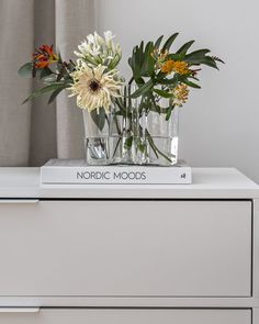 two vases filled with flowers on top of a white dresser