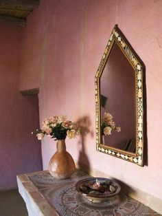 a vase with flowers sitting on top of a table next to a mirror and wall