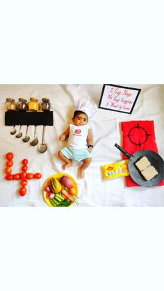 a baby is laying on the bed with food and utensils around him,