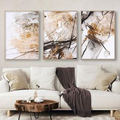 three abstract paintings hang on the wall above a white couch and coffee table in a living room