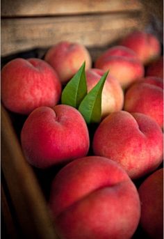 there are many peaches in the basket with leaves on top and one has a green leaf sticking out of it