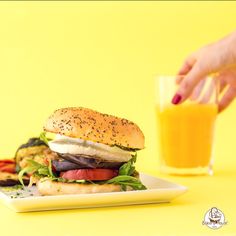 a hand reaching for a sandwich on a plate next to a glass of orange juice