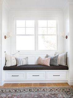 a window seat with pillows on it in front of a rug and windowsills