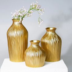 three gold vases with white flowers in them