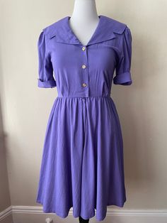 "Vintage 90s polyester rayon blend short sleeve purple dress. Button and zip up front, cuffed sleeves, pockets, shoulder pads. A-line, secretary style dress.  Please ask questions!  Measurements (laid flat):  Tag Size: 10 Pit to Pit: 18.5\"x2 Waist: 14\"x2 Hips: 29\"x2 Condition: Great vintage condition, no issues noted.  The vintage pieces I sell have all led a previous life and may tell their stories through minor imperfections. I'll do my best to indicate overall condition, but please refer to the pictures. Your purchase continues the life of this garment...what stories will you tell while wearing it?  Please note there may be a slight difference in color when comparing the actual garment to the monitor image. (0558)" Purple Collared Summer Dress, Purple Short Sleeve Dress With Buttons, Vintage Purple Dress With Short Sleeves, Fitted Purple Collared Dress, Purple Fitted Collared Dress, Vintage Purple A-line Dress, Vintage Purple Knee-length Dress, Fitted Purple 1970s Style Dress, Purple Button-up Dress For Daywear