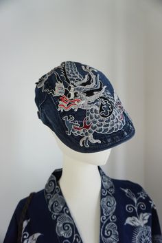 a blue hat with white dragon embroidered on the front and side, next to a mannequin's head