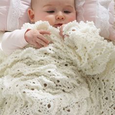 a baby wrapped in a white crochet blanket laying on top of a bed