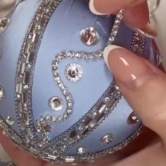 a person holding a blue ornament with diamonds on it's face and nails