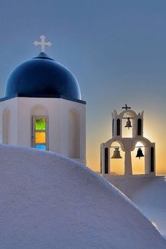 two white and blue buildings with bells in the snow at sunset or dawn, one has a stained glass window