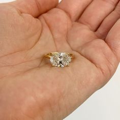 a person's hand holding an engagement ring with two diamonds on top of it