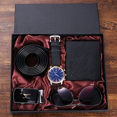 a watch, sunglasses, belt and other items in a black box on a wooden table