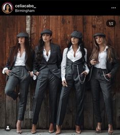 three beautiful women standing next to each other in front of a wooden wall wearing suits and hats