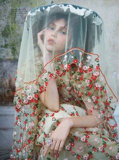 a woman wearing a veil with flowers on it and holding her hand to her face