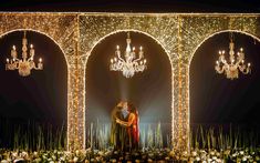 a couple standing in front of an archway with chandeliers