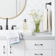 a bathroom sink with two towels hanging on it's side and a round mirror above it