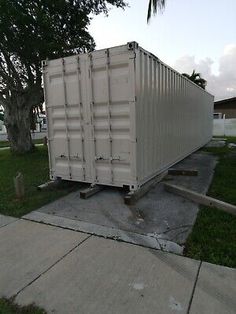 a white container sitting on top of a sidewalk next to a tree and grass field