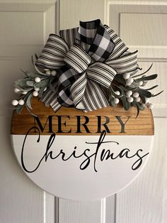 a merry christmas sign hanging on the front door with a wooden board and ribbon attached to it