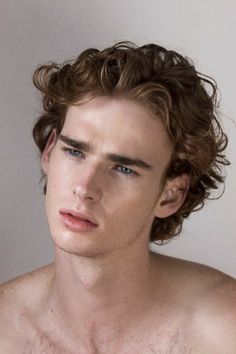 a young man with curly hair and no shirt is looking at the camera while he has his eyes closed